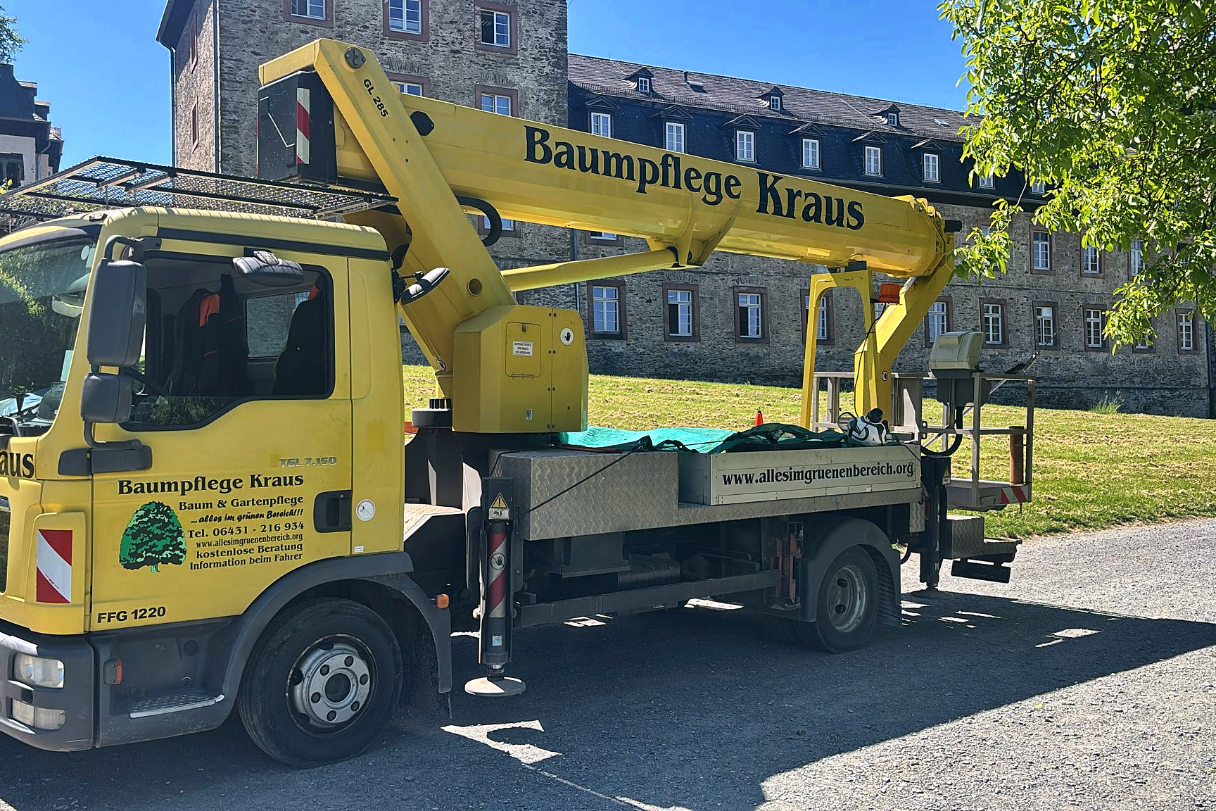 Gelbe Lkw-Hubarbeitsbühne von Baumpflege Kraus vor einem historischen Natursteingebäude.