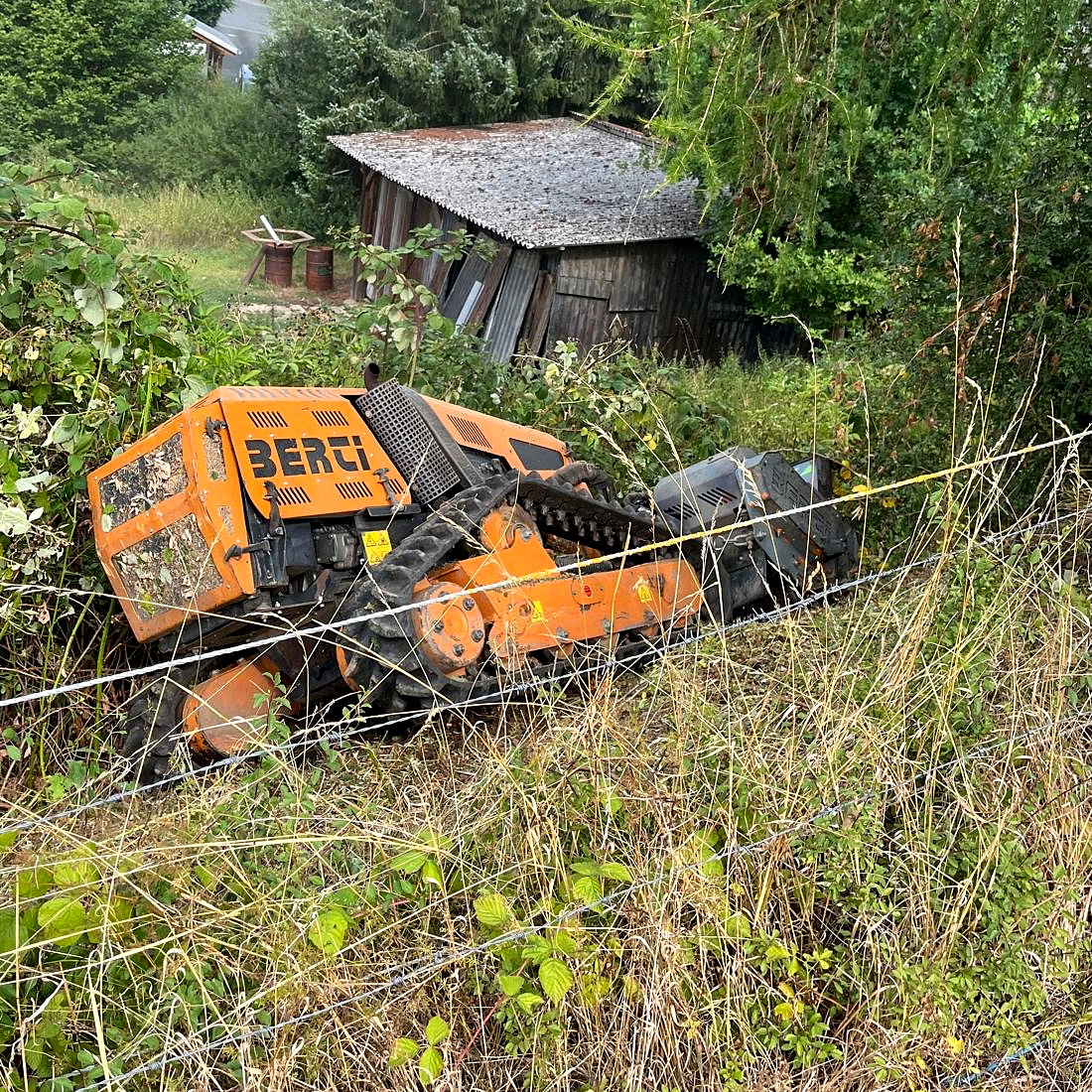 BERTI-Mulchraupe bearbeitet eine dicht bewachsene Hangfläche neben einem Gartenhaus