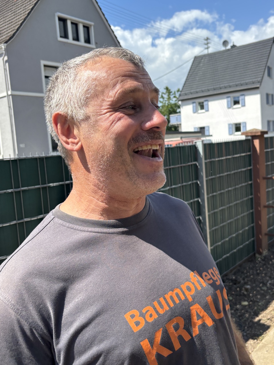 Lachender Mitarbeiter der Baum- und Gartenpflege Kraus in einem Arbeitsshirt auf einer Baustelle