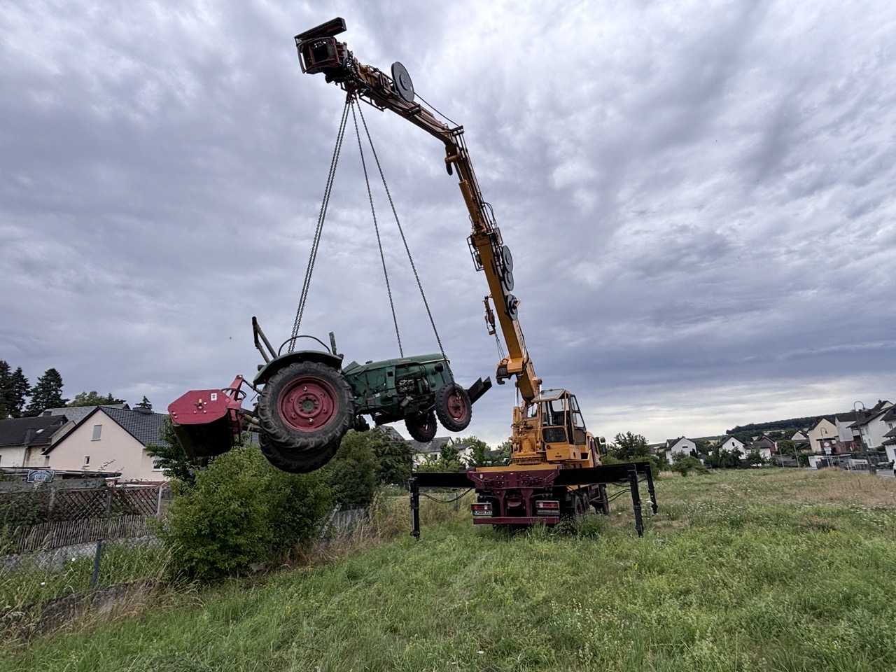 Kran der Baum- und Gartenpflege Kraus hebt einen Traktor mit Anbaugerät in einen schwer zugänglichen Bachlauf