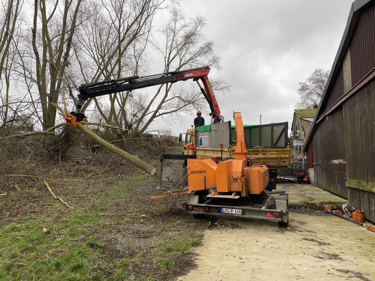 Lkw-Kran mit Holzgreifer bei der Beschickung eines Holzhäckslers.