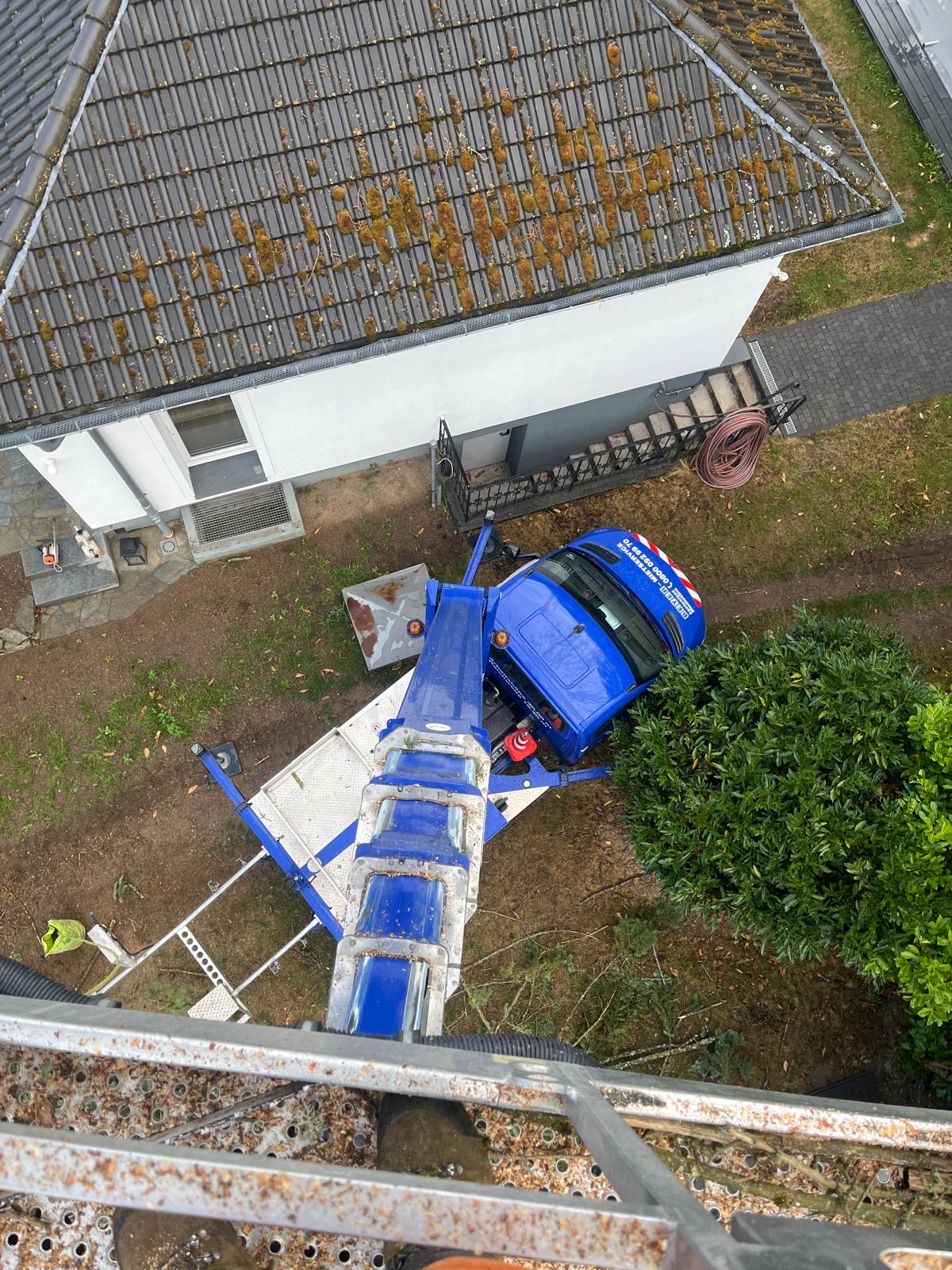 Blick aus dem Arbeitskorb einer Hubarbeitsbühne auf das abgestützte Fahrzeug neben einem Gebäude.