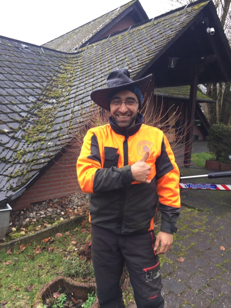 Lachender Mitarbeiter der Baum- und Gartenpflege Kraus in orangefarbener Arbeitskleidung zeigt während eines Einsatzes den Daumen nach oben